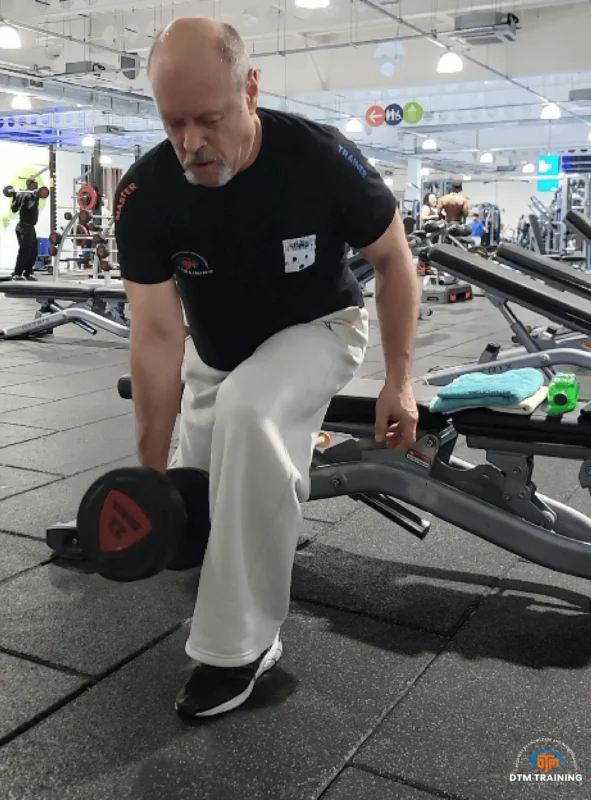 Daniel Batir performing a Bulgarian split squat with a dumbbell in a commercial gym, demonstrating lower-body strength and functional training.