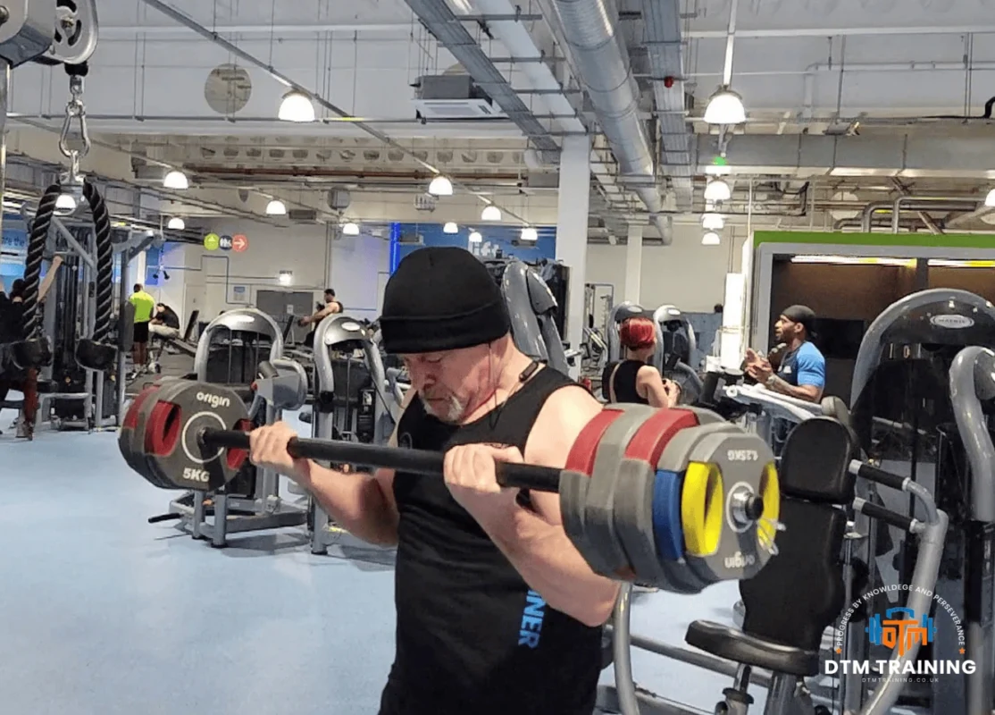 Daniel Batir performing a heavy barbell curl during a strength training session in a commercial gym.