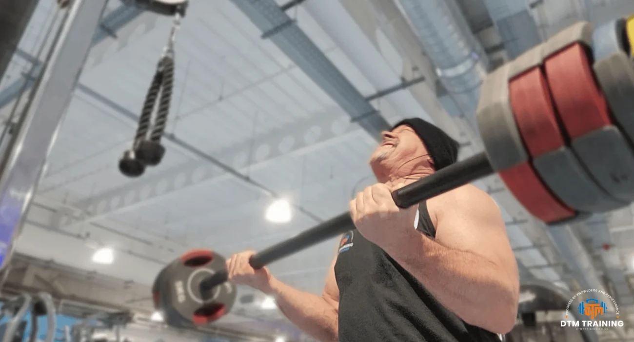 Daniel Batir performing a barbell curl exercise during a strength training session in a commercial gym.