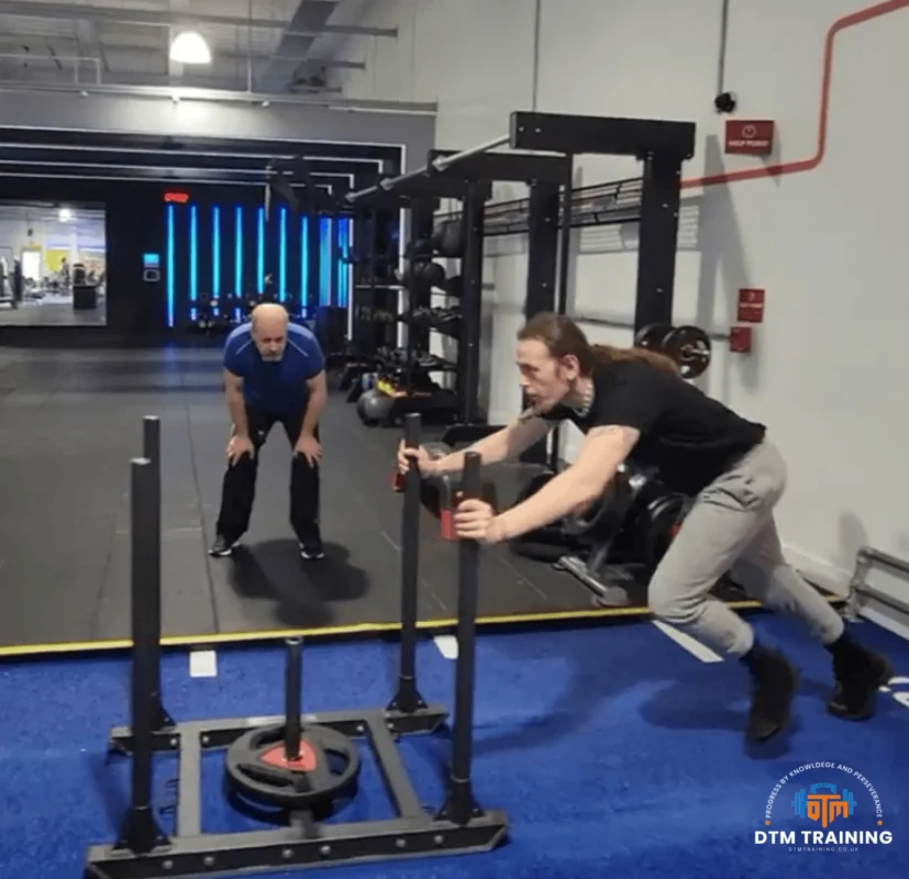 Daniel Batir coaching a client during a weighted sled push exercise, providing guidance on technique, effort, and conditioning performance.
