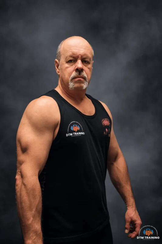 Daniel Batir, founder of DTM Training, standing in a studio portrait with a confident and professional posture against a dark textured background.