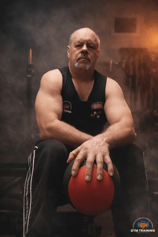 Daniel Batir, founder of DTM TRAINING, seated with a medicine ball during a strength and conditioning portrait session in London.