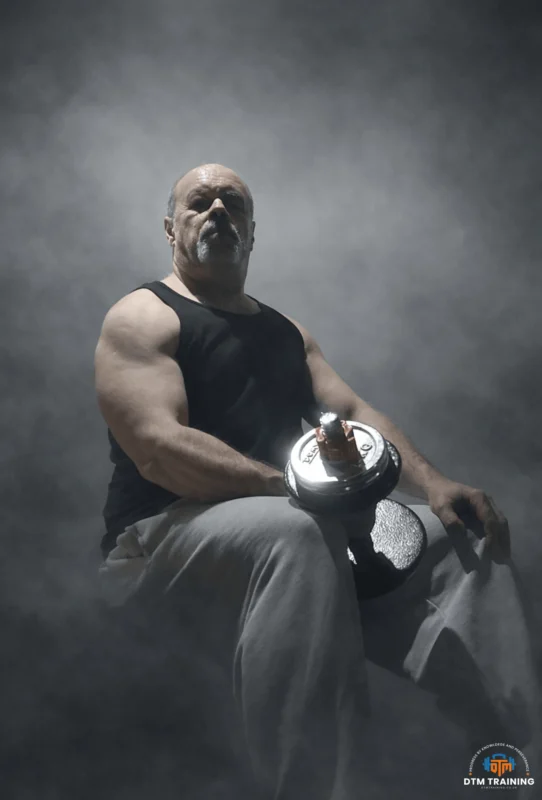 Daniel Batir holding a dumbbell during a dramatic strength training portrait, representing personal training, muscle development, and strength coaching in London.