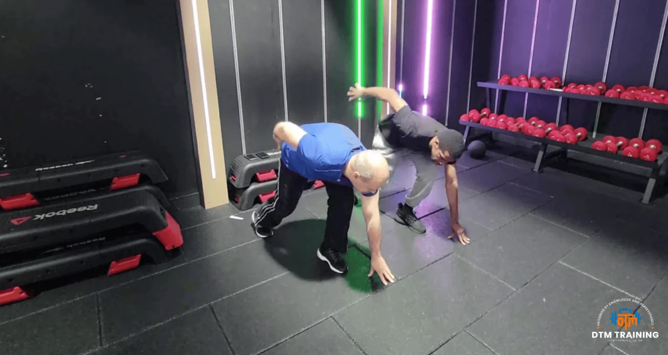 Daniel Batir demonstrating a functional mobility exercise alongside a client during a personal training session in London.