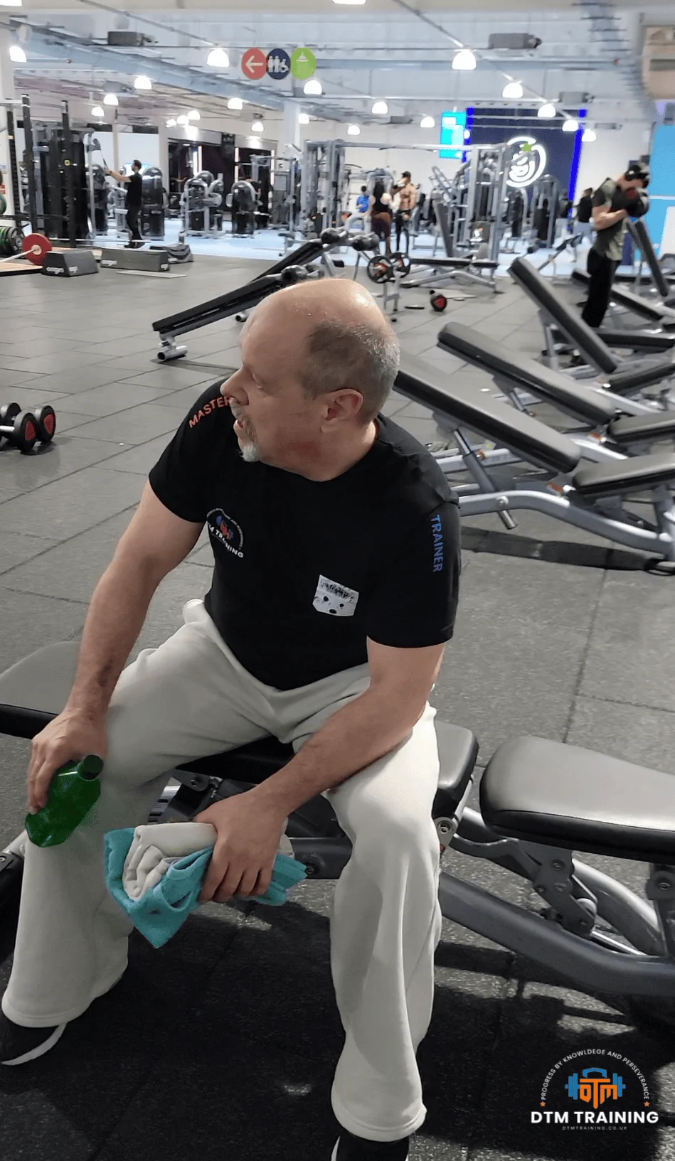 Daniel Batir, personal trainer and strength coach, seated on a gym bench during a training session in a commercial gym environment.