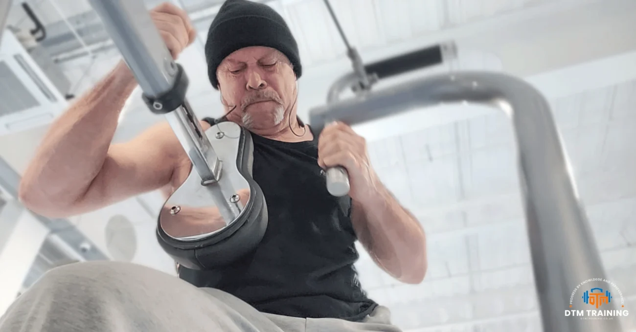 Daniel Batir performing a high-intensity upper-body exercise on a resistance machine in a commercial gym in London.