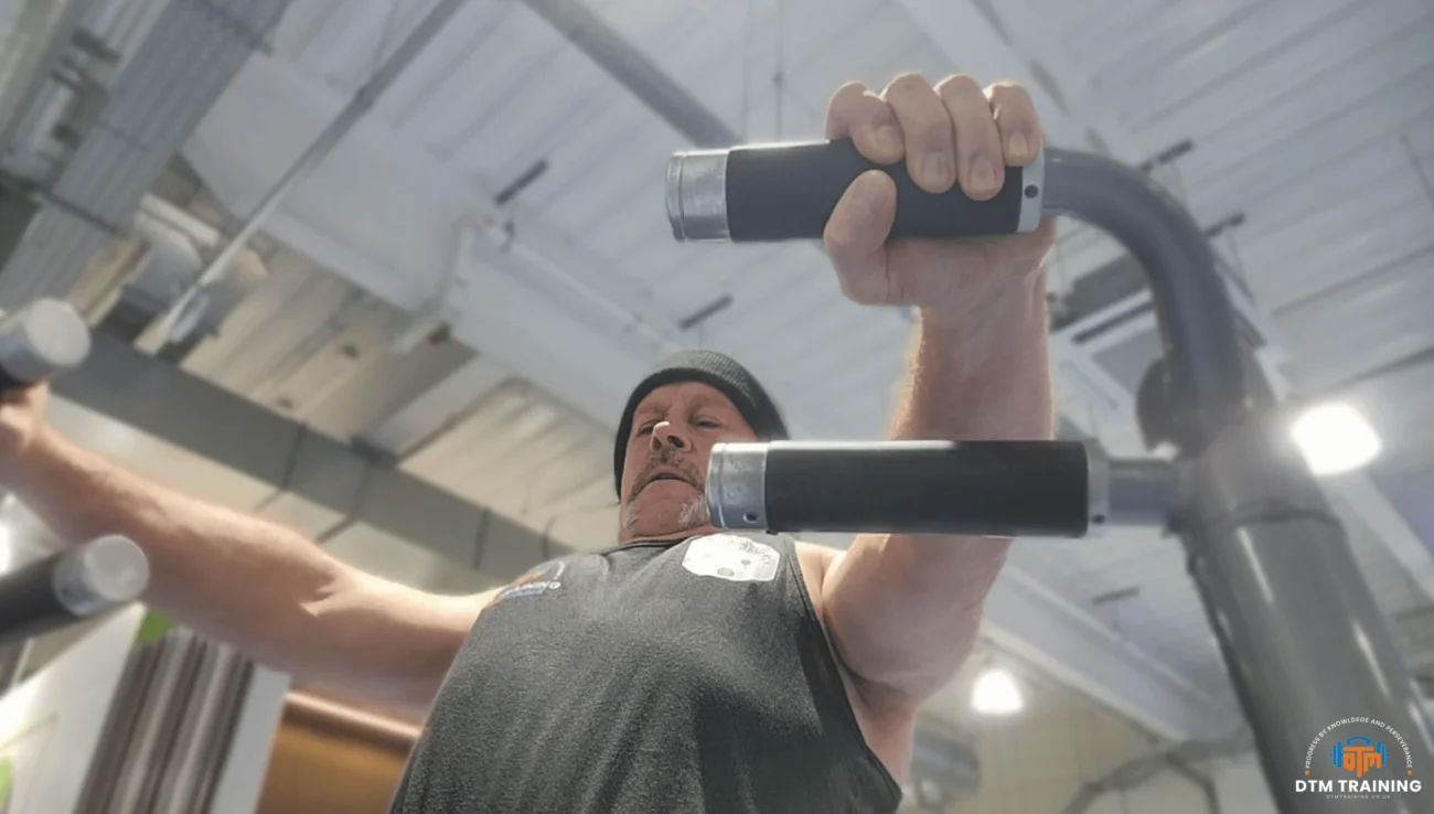 Daniel Batir performing a machine chest press exercise in a commercial gym, demonstrating upper body strength training and controlled movement technique.