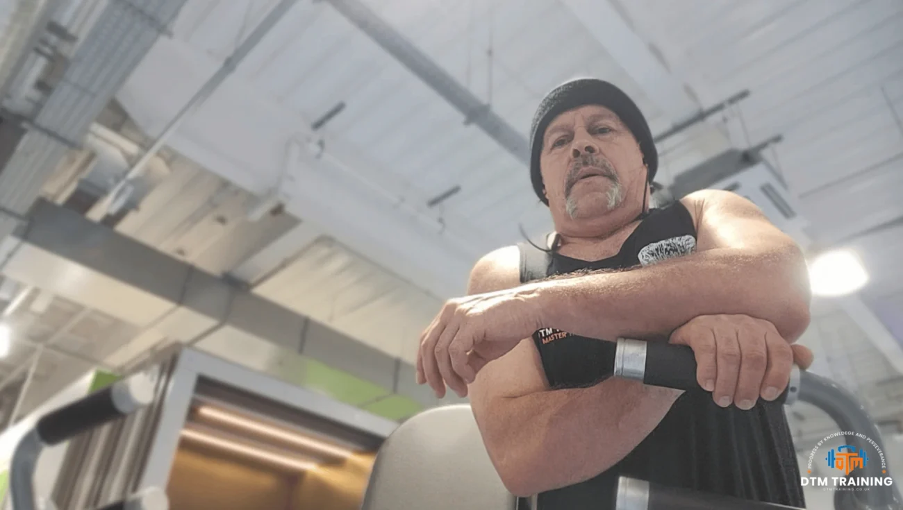Daniel Batir observing a training session from a strength machine while monitoring exercise technique and performance in a London gym.