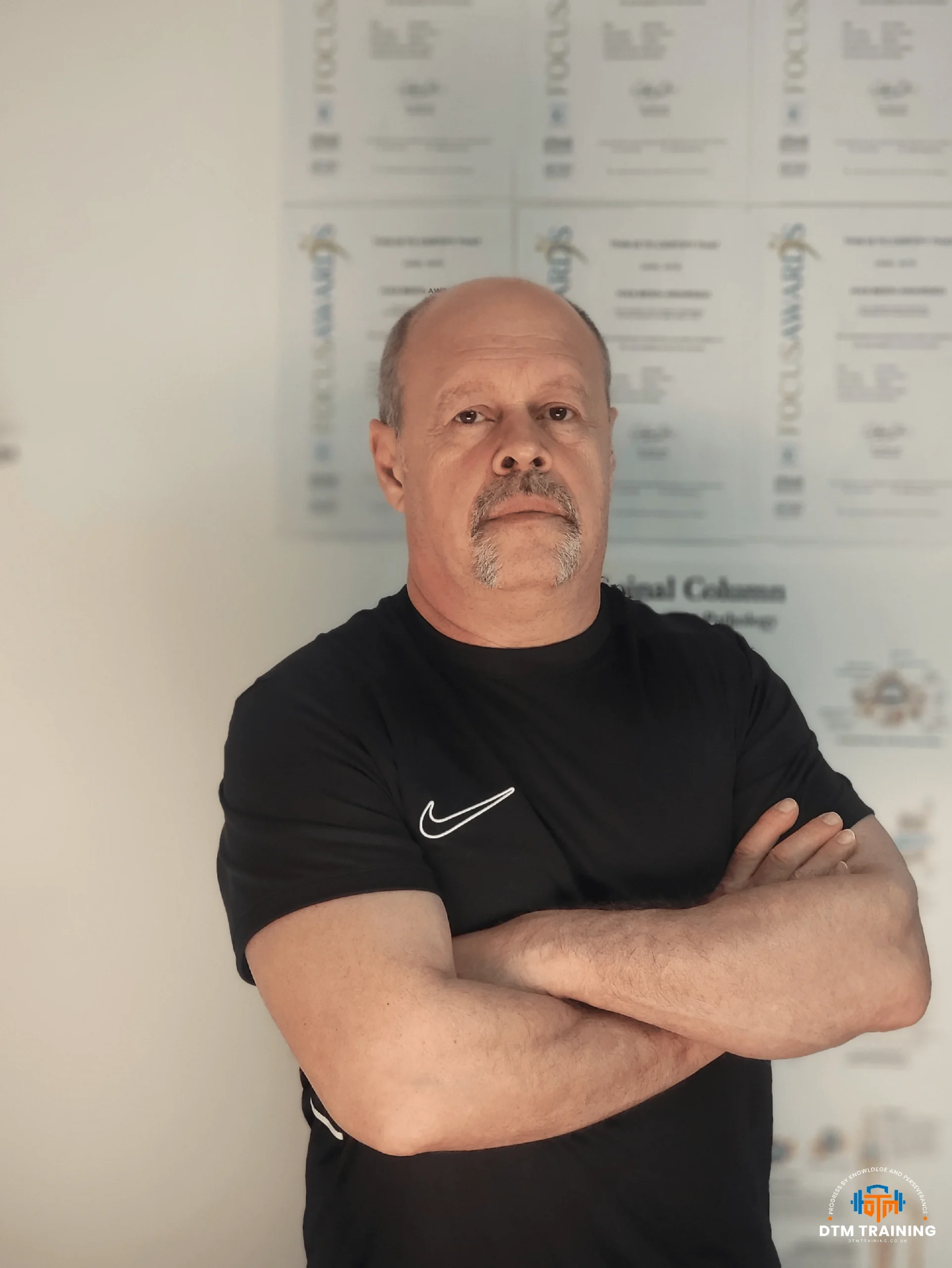 Daniel Batir, qualified personal trainer and sports massage therapist, standing in front of professional fitness and coaching qualifications.