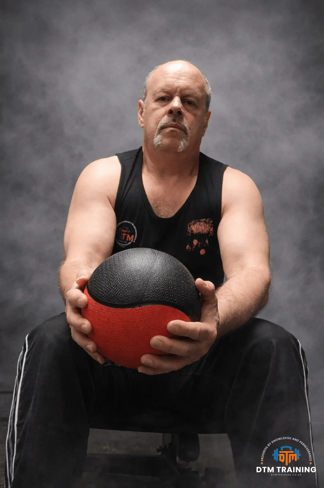 Daniel Batir holding a medicine ball during a strength and conditioning session, seated against a dark studio-style background.