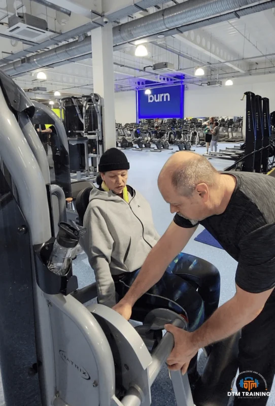 Daniel Batir coaching a client on a leg extension machine during a personalised personal training session in a commercial gym.