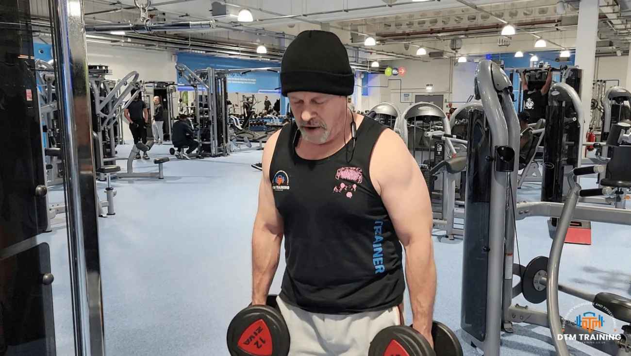 Daniel Batir performing a dumbbell strength training exercise in a commercial gym in London.