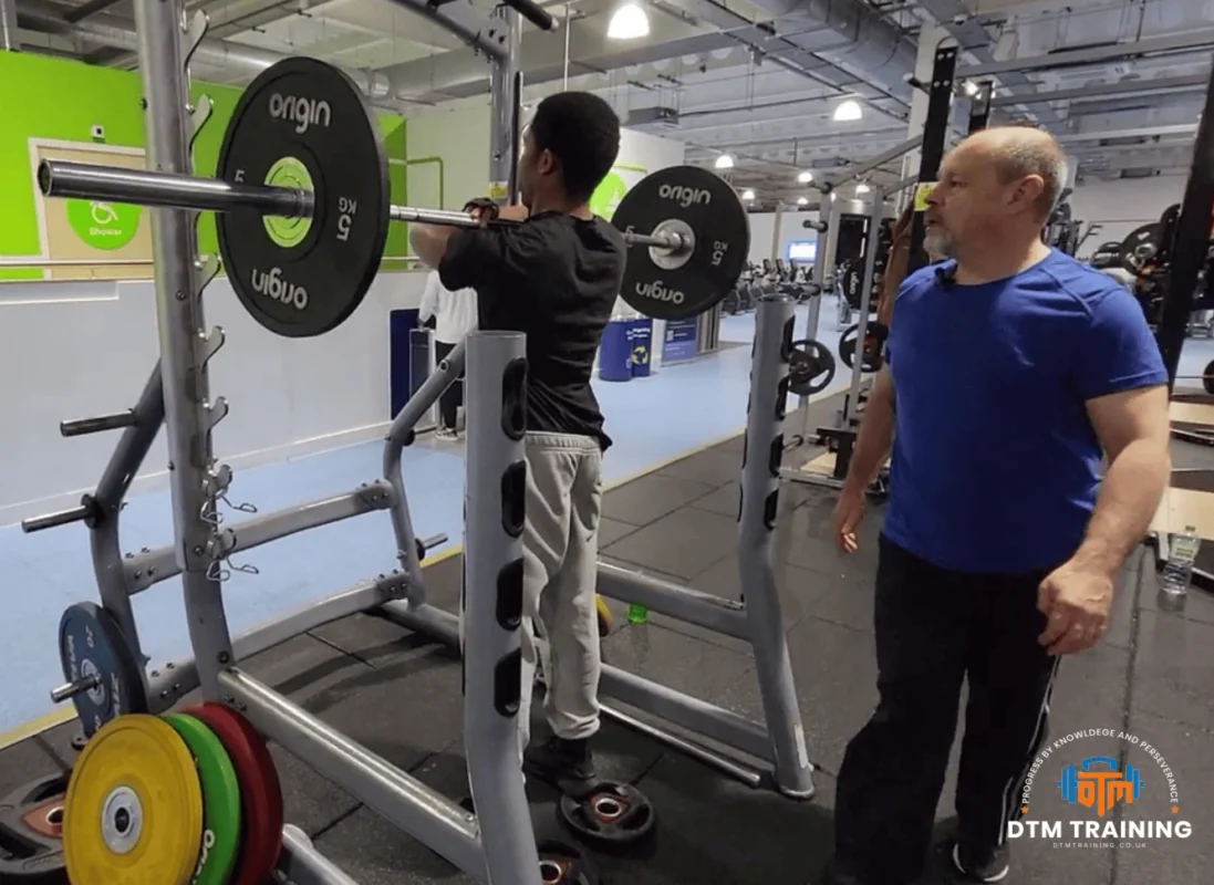 Daniel Batir coaching a client during a barbell front squat exercise in a London gym.
