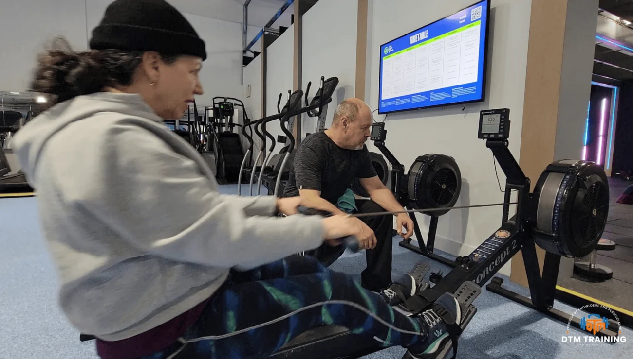 Daniel Batir coaching a client during a rowing machine conditioning session in a London gym.